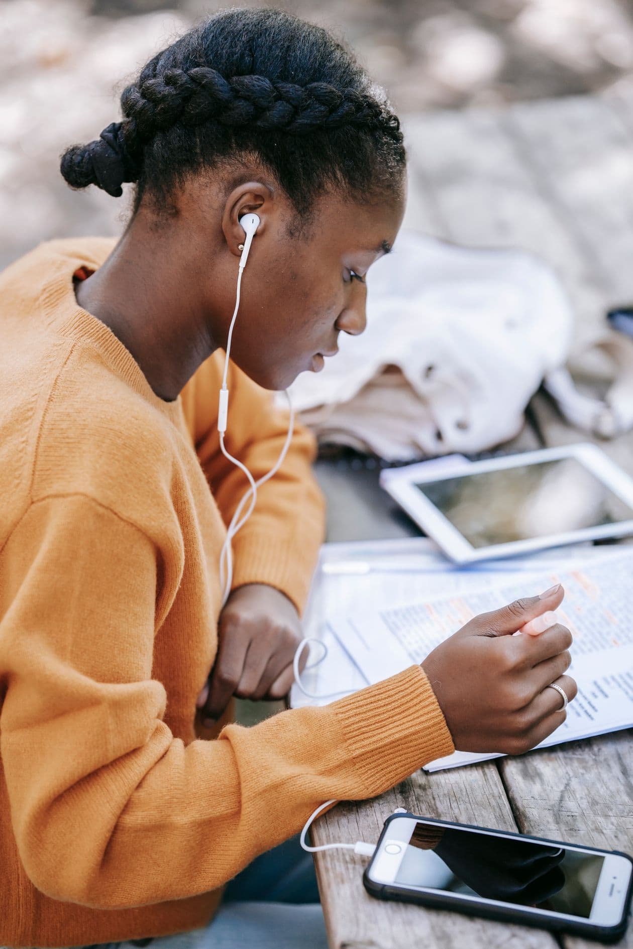 A student in an orange jumper studies from printed notes with her phone on the table